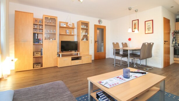 Una sala moderna con televisor, muebles de madera, un comedor con sillas y una pequeña mesa con un tapete.
