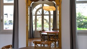 A dining area with a wooden table and chairs, a large ornate mirror, and a view of the outdoors through a window.