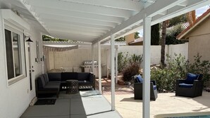 Un patio couvert avec une piscine, des sièges d’extérieur et un barbecue.