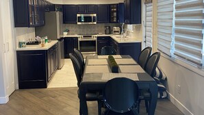 Une cuisine moderne avec des meubles de couleur sombre, un îlot central et un coin repas comprenant une longue table et des chaises.