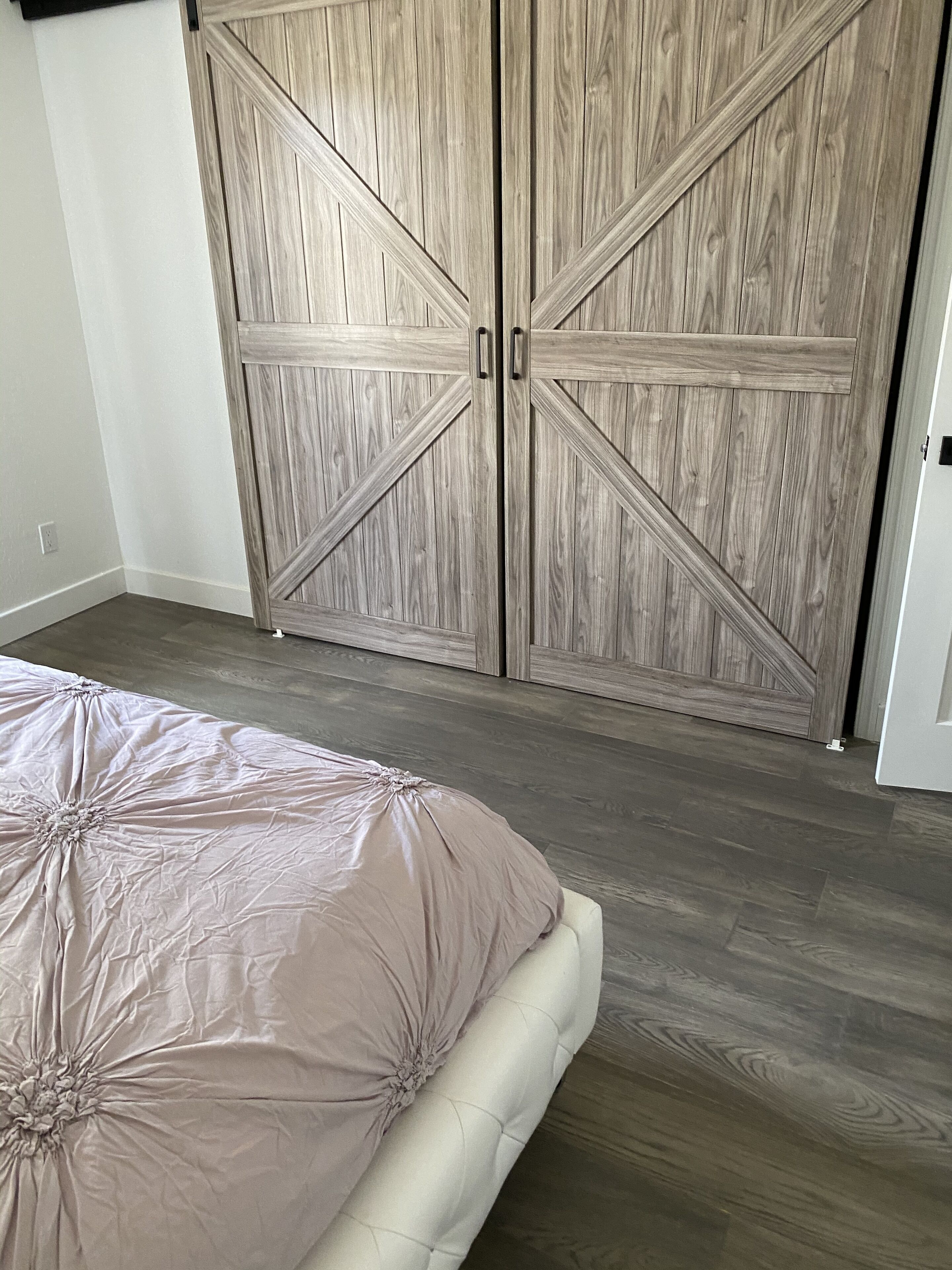 A bedroom with a large wooden wardrobe, a bed with a beige duvet, and a wooden floor.