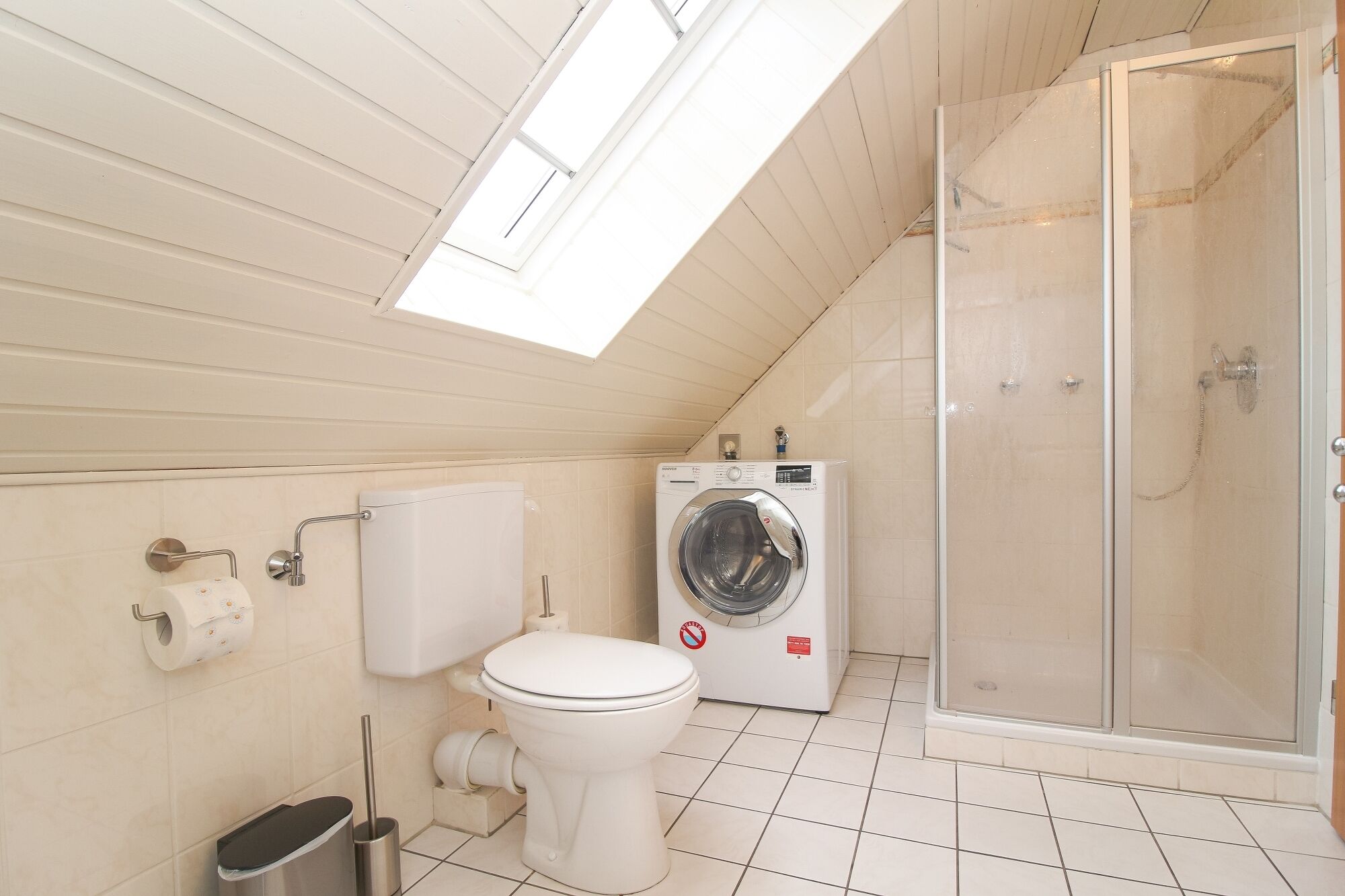 Ein kleines Badezimmer mit Toilette, Waschmaschine und Duschkabine aus Glas.
