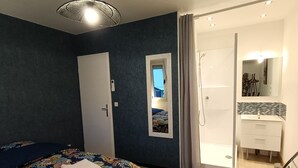 A bedroom with a bed, a wardrobe, a shower area, and a bathroom with a sink and mirror.