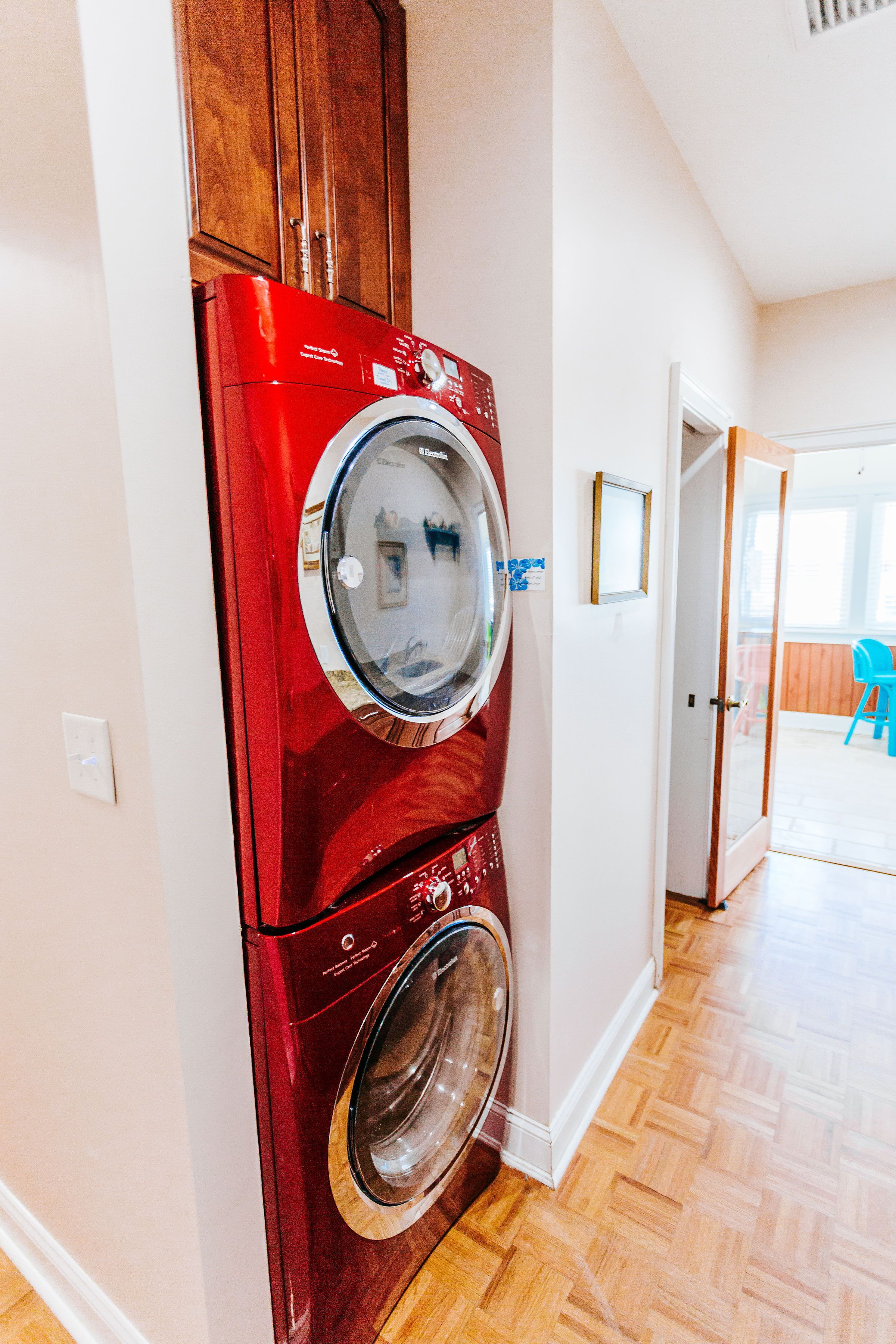 A compact laundry area with a red washing machine and dryer, wooden cabinets, and a wooden floor.