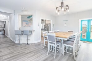 A modern kitchen with white cabinetry, a wooden dining table, and bar stools. - Palazzo 360 5bdr/5 bath with a heated pool sleeps 18 (Murrells Inlet)