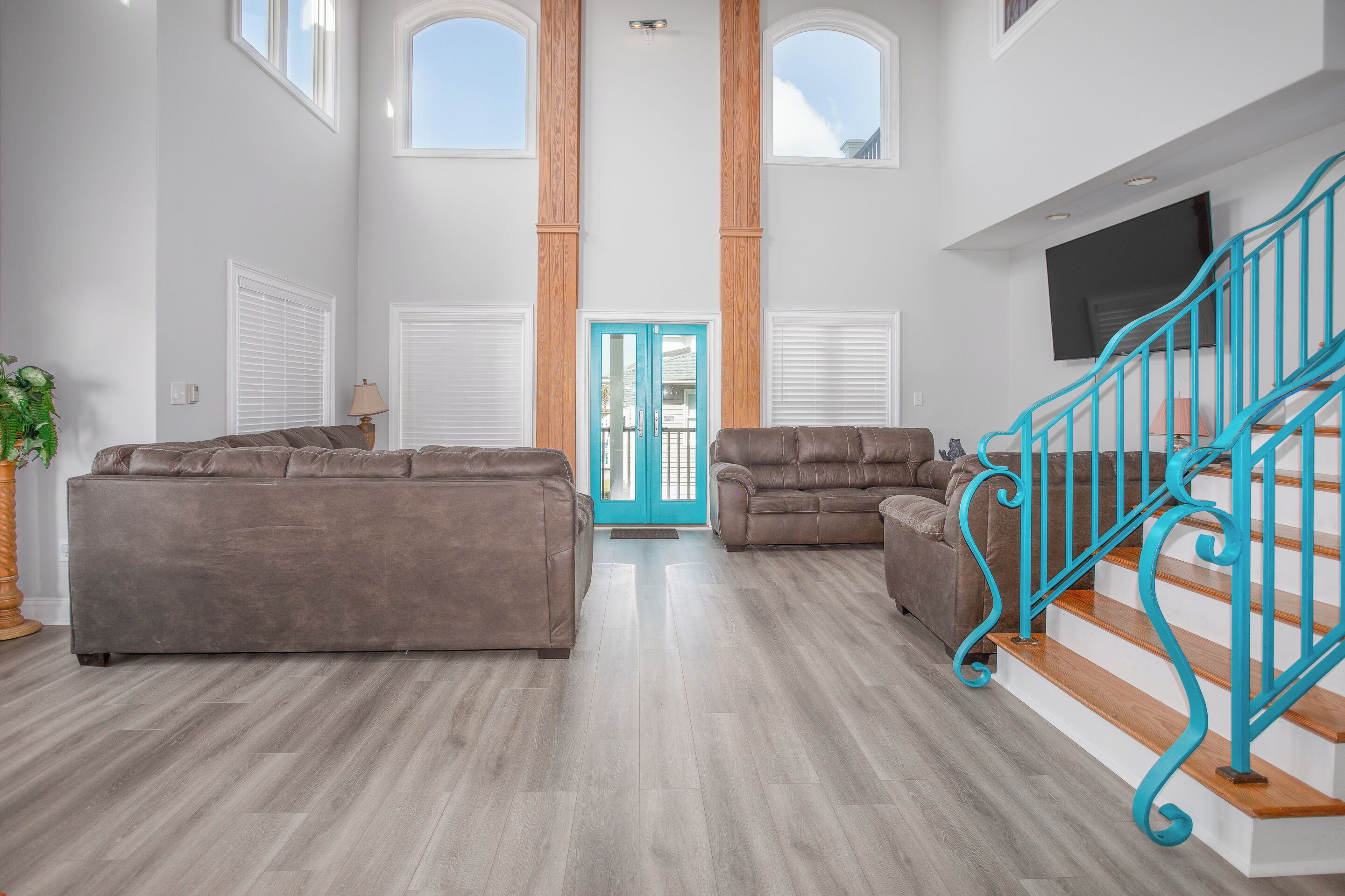 A spacious living room with two sofas, a staircase with turquoise railings, and a large window.