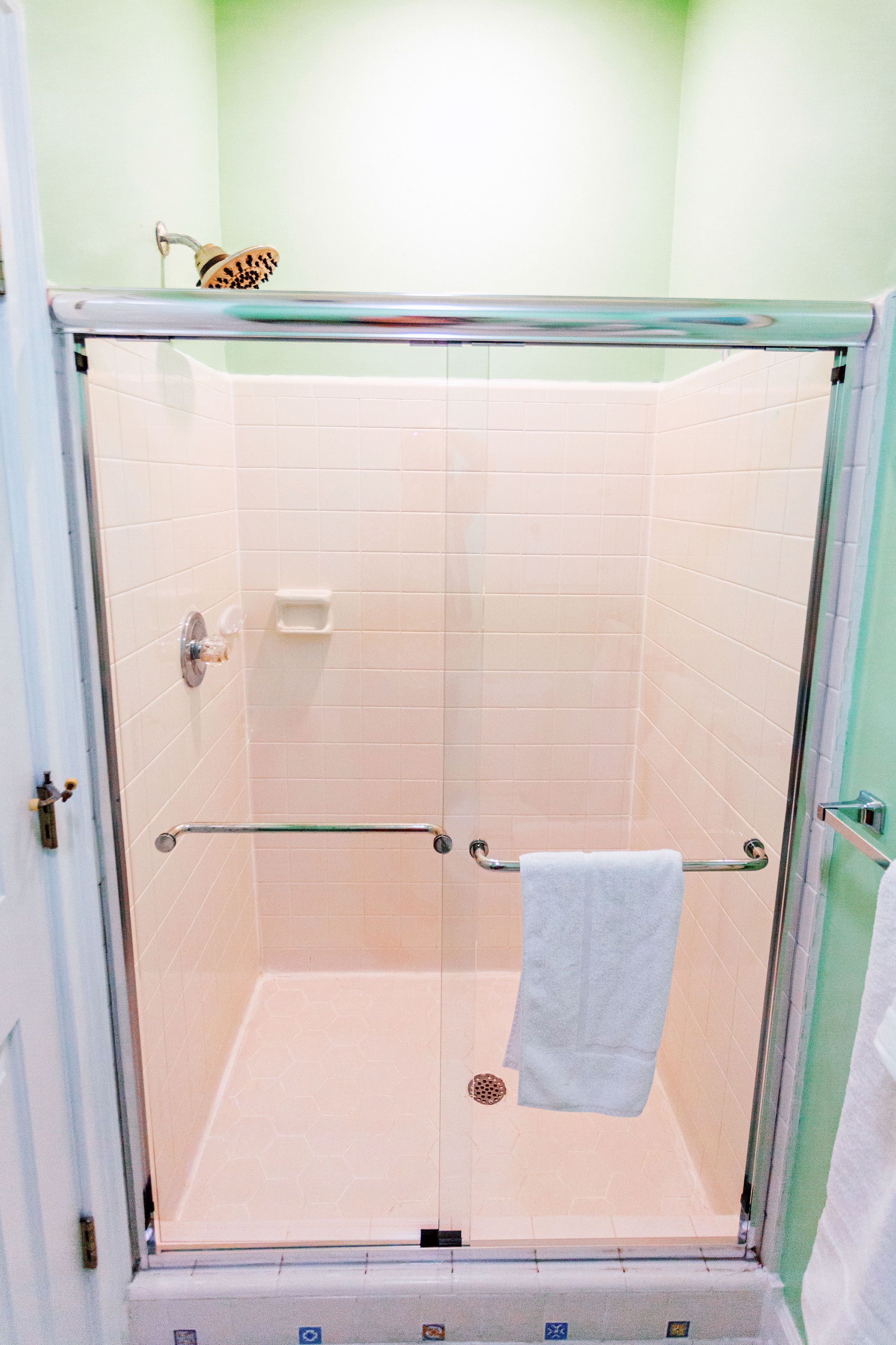 Une douche fermée par des parois en verre, avec une barre d’appui, une serviette accrochée au mur et un petit porte-savon.