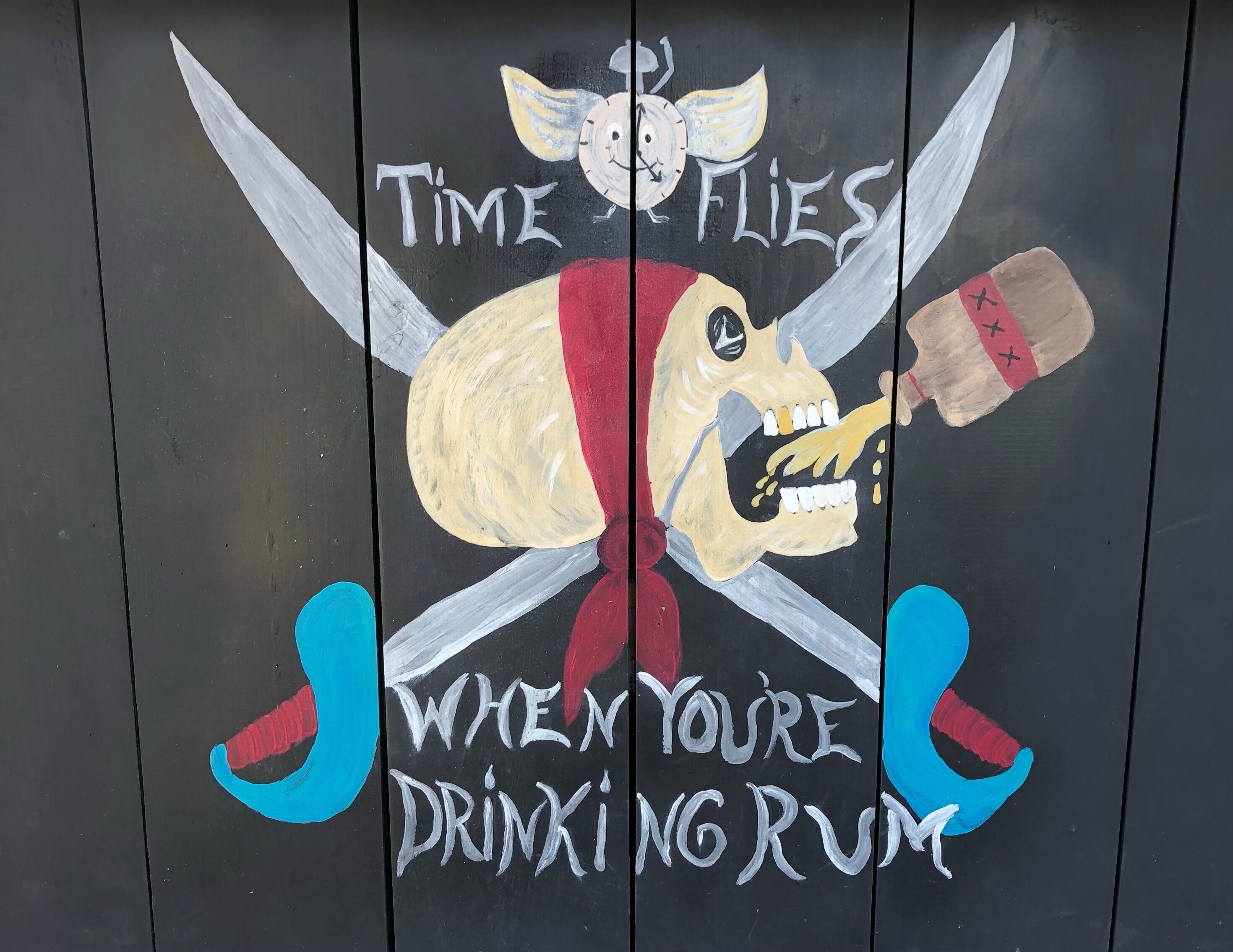 Una pared con una calavera y tibias pintadas, un reloj y texto que dice "El tiempo vuela cuando se bebe ron".