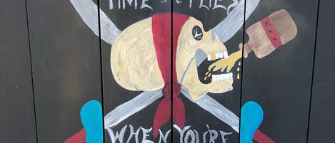Una pared con una calavera y tibias pintadas, un reloj y texto que dice "El tiempo vuela cuando se bebe ron".