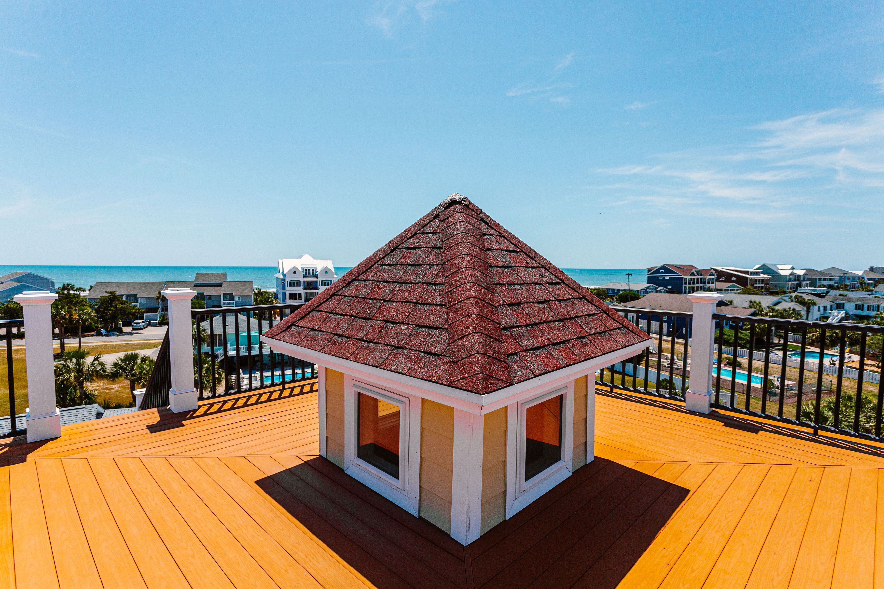 A wooden deck with a small gazebo overlooking a beach and pool area.