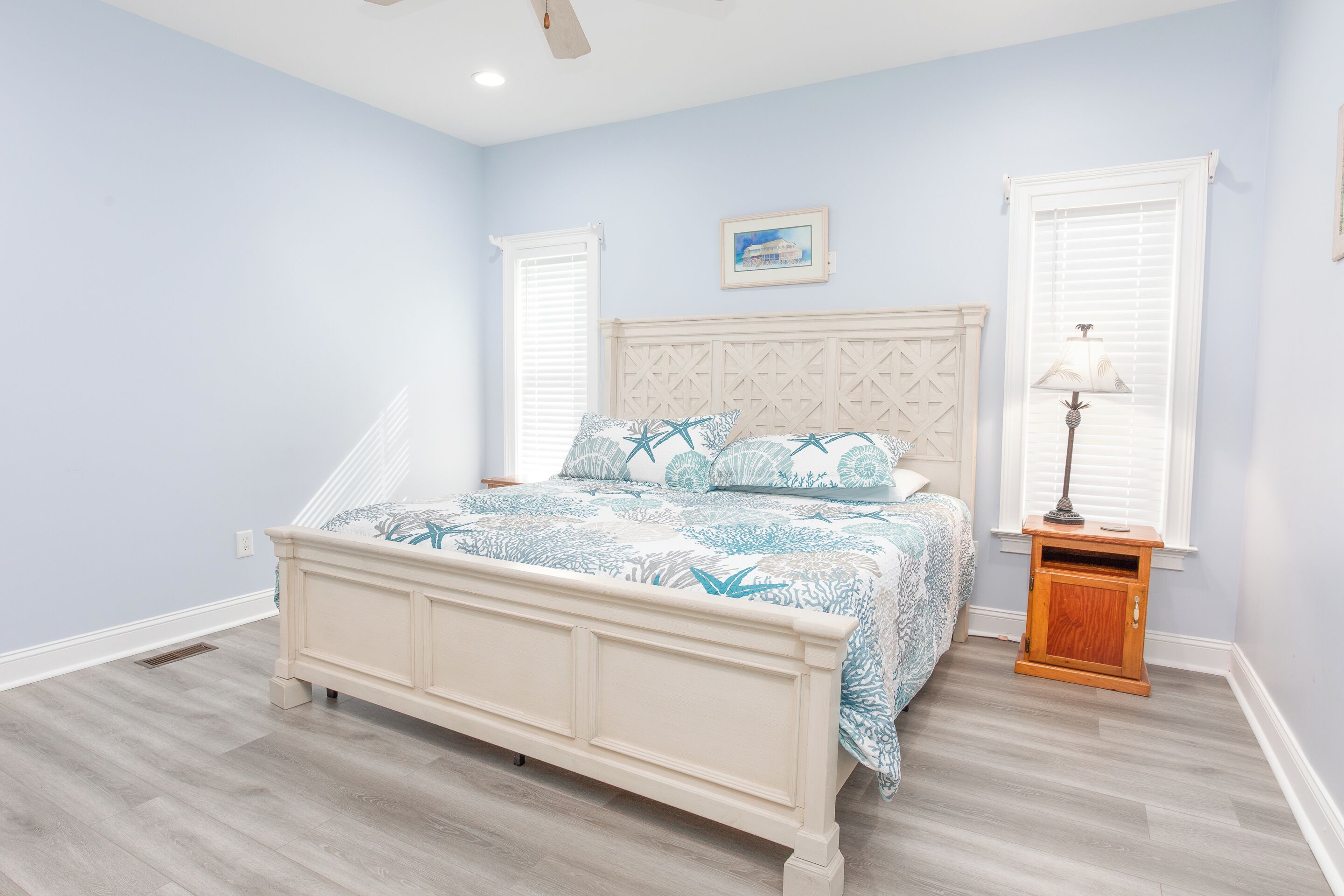 A bedroom with a bed, a nightstand, a wall-mounted lamp, and a window with blinds.