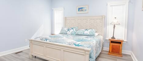 A bedroom with a bed, a nightstand, a wall-mounted lamp, and a window with blinds.