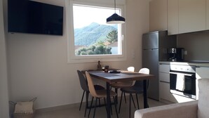 Een kleine keuken met een eettafel, stoelen, een Boeddhabeeld en uitzicht op bergen door een raam.