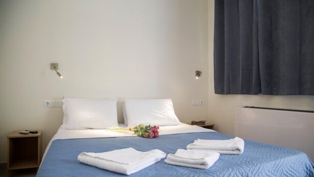 Une chambre d’hôtel avec un lit, deux oreillers, une couvre-lit bleue, un bouquet de fleurs et deux serviettes pliées.