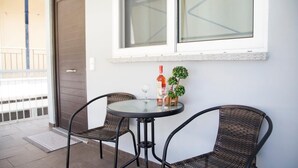 Un petit espace extérieur aménagé avec deux chaises en osier et une table ronde, une bouteille de vin et une petite plante en pot.