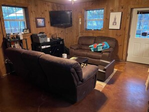 Ein gemütliches Wohnzimmer mit einer braunen Ledersofa, einem Wand-Fernseher und einem Fenster mit Jalousien.