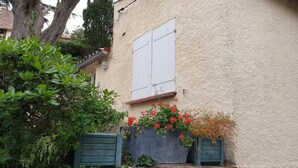 A house with a textured exterior, a white window, and a green door. There are potted plants with red flowers in front of the house. - Mazet Provençal Avec Magnifique vue mer (Sainte-Maxime)