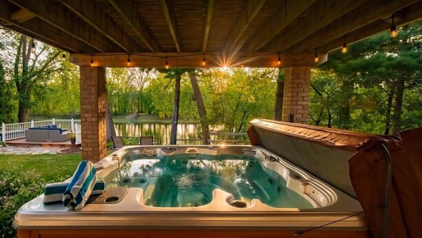 Un jacuzzi bajo una pérgola de madera con vista a un lago y árboles.