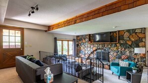 Una sala de estar con pared de piedra, chimenea, televisor y sofá azul.