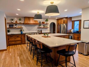 A modern kitchen with wooden cabinets, a marble island, bar stools, and a stainless steel refrigerator.