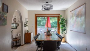 Un comedor con una larga mesa de madera, sillas negras, un paraguas rojo y vistas al exterior con vegetación.