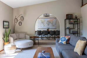 Un salon comprenant un canapé, une table basse, une table à manger avec des chaises, une carte accrochée au mur et une bibliothèque.