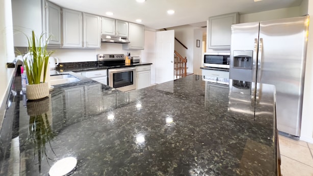 A modern kitchen with stainless steel appliances, a marble countertop, and white cabinetry.