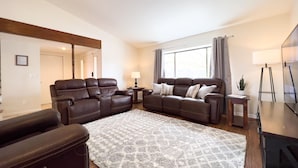 A living room with a brown leather sofa set, a patterned rug, and a television on a stand.