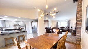 A modern kitchen with stainless steel appliances, a dining area with a wooden table and chairs, and a living room with a sofa and a TV.