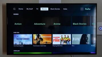 Una pantalla de televisor muestra una interfaz de servicio de transmisión con categorías como Acción, Aventura, Anime, Historias Negras y Clásicos.