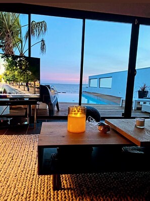 Una sala de estar moderna con un ventanal grande con vista a una piscina y al océano.