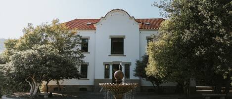 A courtyard with a fountain, a white building with a red-tiled roof, and surrounding trees.