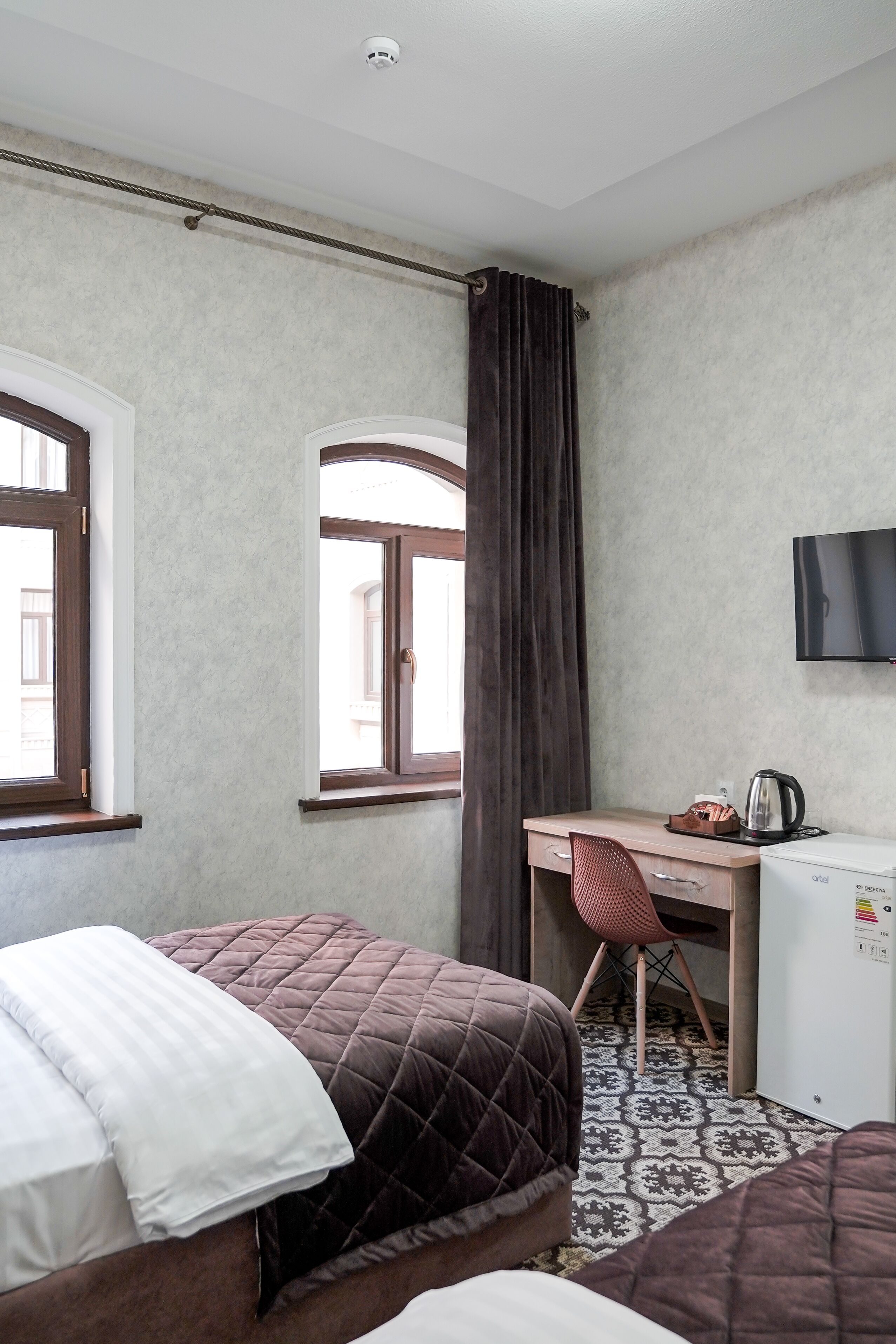 Habitación de hotel con dos camas, un escritorio, una silla, un televisor y un refrigerador pequeño.
