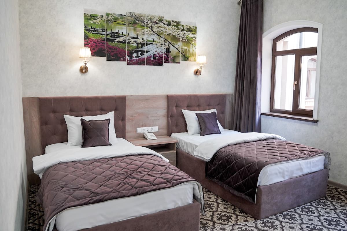 A hotel room with two beds, a large window, and a wall-mounted painting.