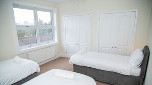 Une chambre avec deux lits simples, une fenêtre donnant sur un immeuble en briques et des armoires blanches.