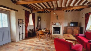 A cozy room with a fireplace, wooden furniture, and a red sofa. - Le domaine des roseraies, gîte Flaubert (Monfréville)