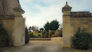 A stone pathway leading through a gate into a landscaped area with trees and shrubs. - Le domaine des roseraies, gîte Flaubert (Monfréville)