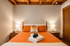 A hotel room with a bed, two bedside lamps, a clock, a pillow with a hot air balloon design, and a towel with a black and white pattern.