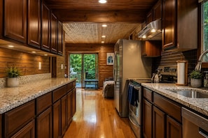 A kitchen with wooden cabinets, granite countertops, stainless steel appliances, and a view to the outdoors.