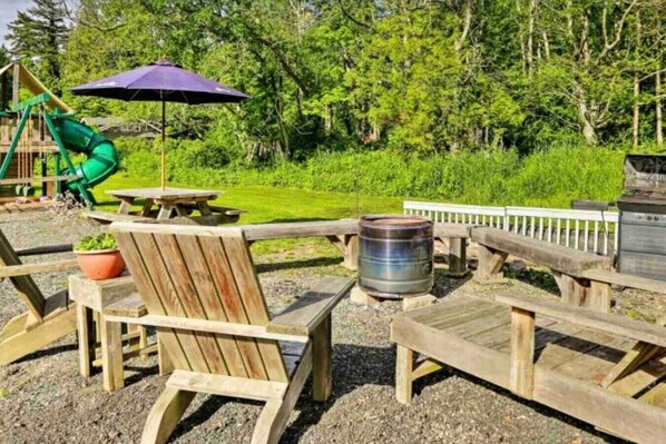 A wooden deck with picnic tables and chairs, a barbecue grill, and a playground with a slide. - The Cowboy cottage  (Bellingham)