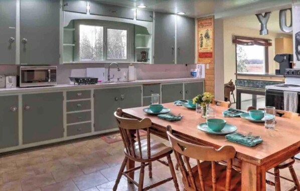 A kitchen with grey cabinets, a wooden dining table with teal placemats, and a stove.