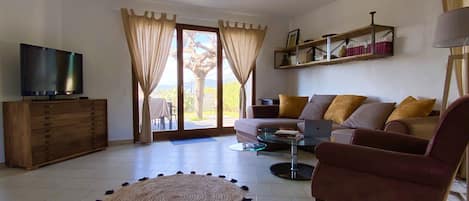 Sala de estar con sofá, sillón, mesa de centro, televisor y vista a través de un ventanal.