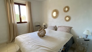 A bedroom with a bed, curtains, a bedside table with a lamp, and wall decor. - House Agosta plage- Terrace with sea view - Sea 500m - 10 people (Albitreccia)