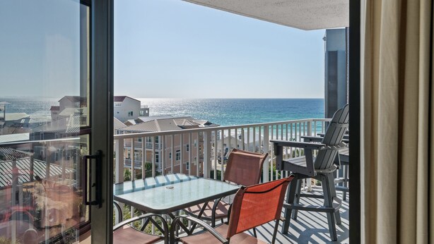 Ein Balkon mit Glastisch und Stühlen, mit Blick auf Strand und Meer.