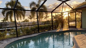 A swimming pool with a curved edge, surrounded by a tiled deck and a glass enclosure.