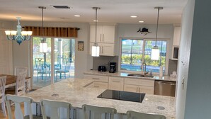 A modern kitchen with a large island, white cabinetry, and a dining area with wooden chairs.