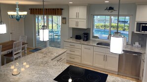 A modern kitchen with granite countertops, white cabinets, a stainless steel dishwasher, and a dining area with blue chairs.