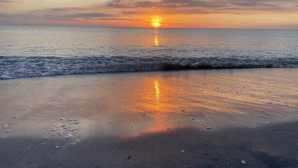 A beach with a sunset over the ocean, waves gently lapping at the shore.