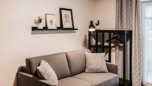 A living room with a sofa, decorative pillows, a wall-mounted shelf with framed pictures and a vase, a floor lamp, and patterned curtains. - schoene Ferienwohnung-Wagrain (Wagrain)