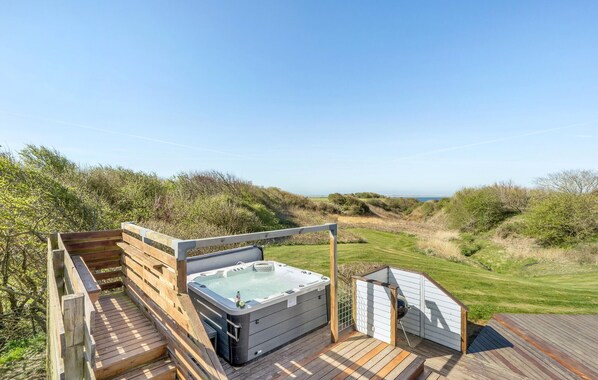 Eine Holzterrasse mit Whirlpool und Grillplatz mit Blick auf eine grüne Landschaft und das Meer.